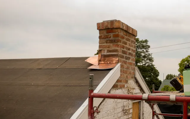 Example photo: Black felt underlayment laid in overlapping courses on a roof deck beside a brick chimney